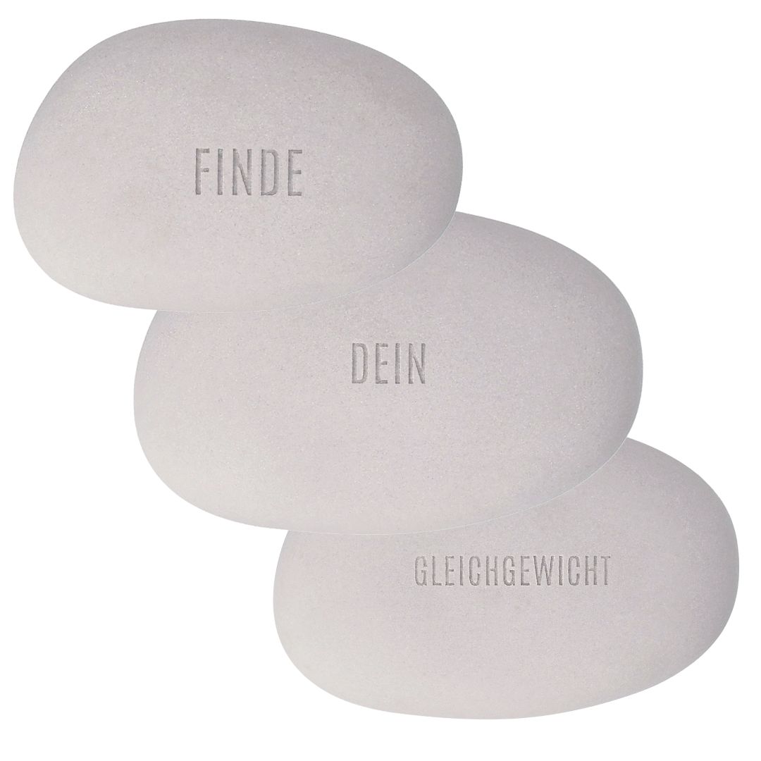 Nahaufnahme der Relief-Schriftzüge Finde, dein und Gleichgewicht auf den grauen Kieselsteinen