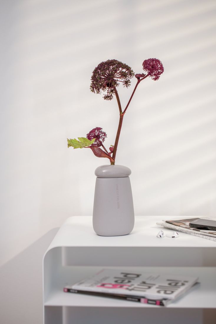Graue Kiesel-Vase von räder mit einer zarten Blume als Motivationsgeschenk auf dem Schreibtisch