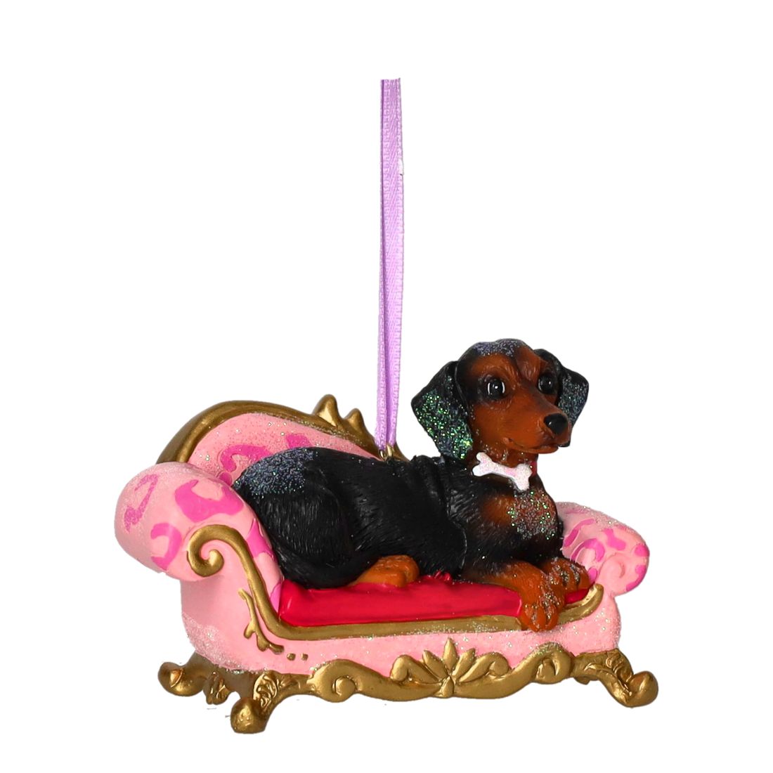 Schwarz-brauner Dackel entspannt auf einem glitzernden rosa Sofa mit goldenen Verzierungen und weißem Knochen-Kollier als Weihnachtsbaumanhänger