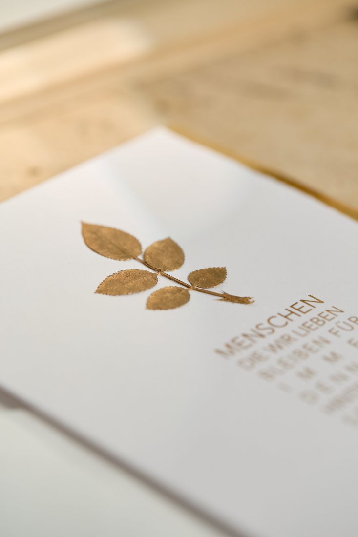 Nahaufnahme der räder Goldblatt Beileidskarte mit Fokus auf das filigrane echte Blatt und die schimmernde Heißfolienprägung