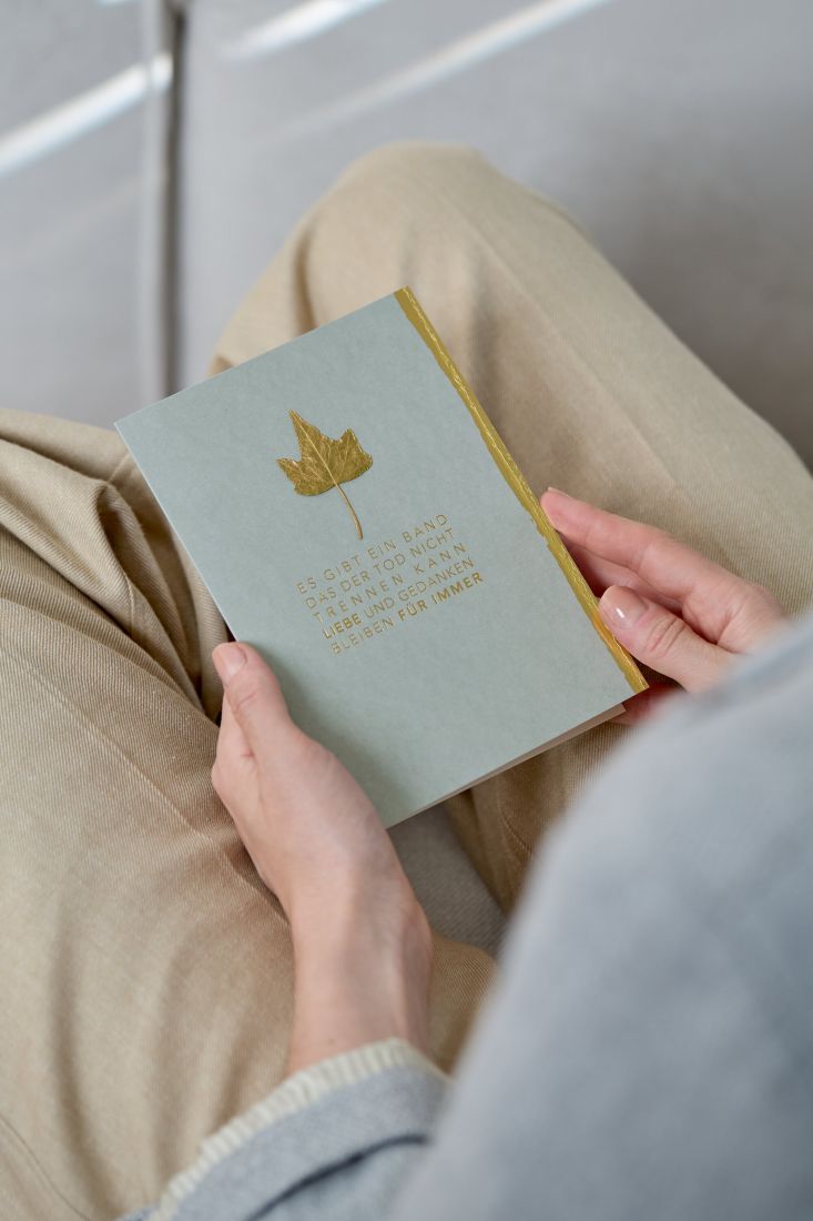 grauen räder Beileidskarte mit Fokus auf das filigrane echte Blatt und die goldene Prägung