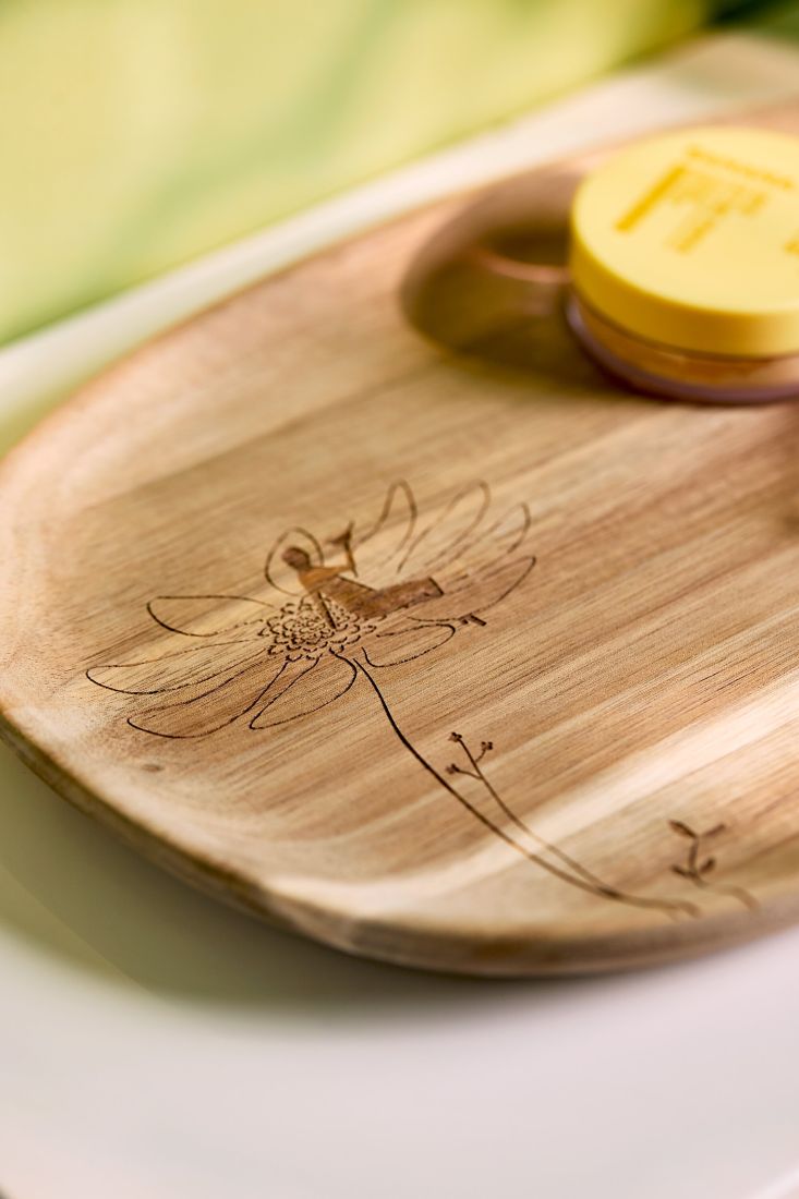 Nahaufnahme der feinen gelaserten Illustration einer Figur auf einer Blüte auf dem räder Akazienholz-Tablett