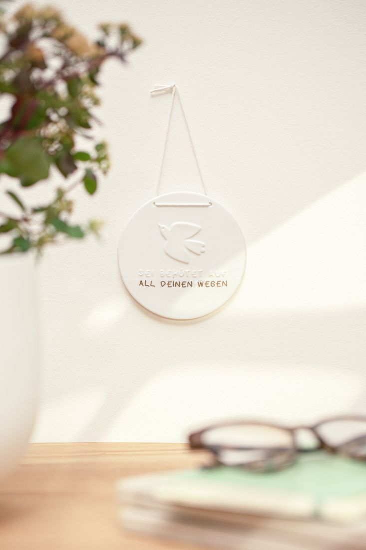 An einer hellen Wand hängendes Porzellanschild mit Tauben-Motiv