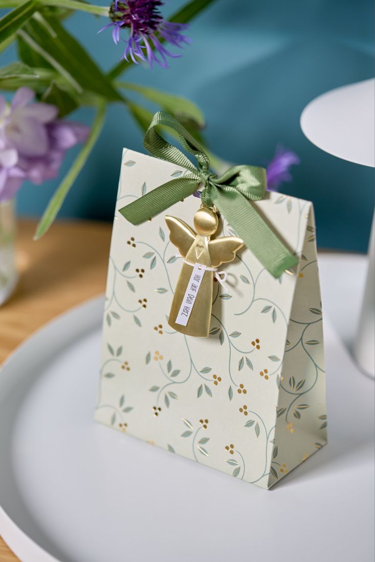 Der goldene räder Metall-Engel liebevoll als glänzender Anhänger an einer edlen Geschenkschleife dekoriert