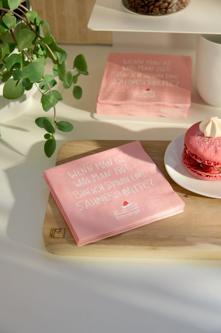 Nahaufnahme der kleinen räder Papierserviette Sahneschnitte humorvoll dekoriert auf einem Kuchenteller neben einem Stück Torte