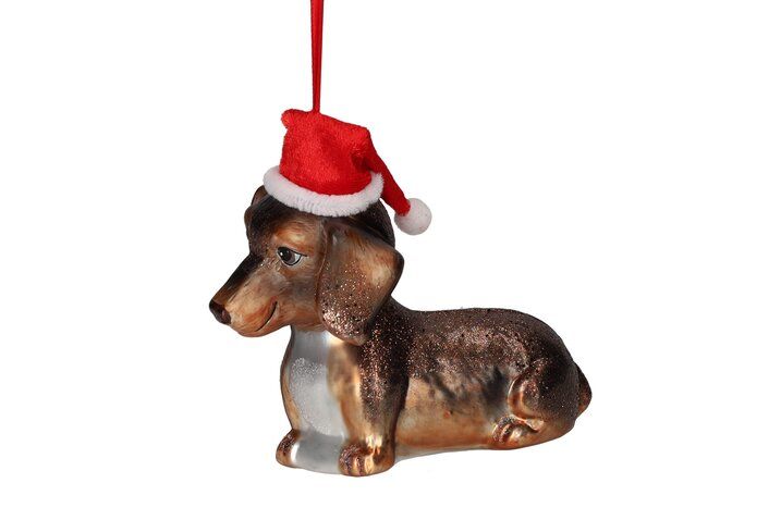 Liegender brauner Dackel aus Glas als Weihnachtsbaumanhänger mit kleiner roter Nikolausmütze, feinen Glitzer-Akzenten und rotem Aufhängeband